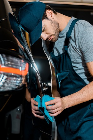 Young auto mechanic cleaning car with rag at auto repair shop