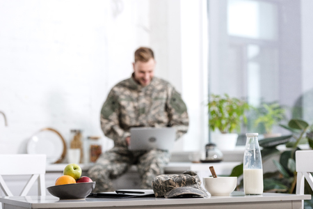 selective focus of army soldier working on laptop in kitchenの写真素材