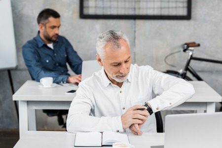 Handsome businessman checking time on wristwatch in office