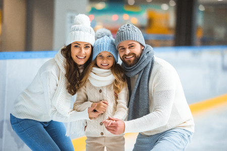 Portrait of cheerful parents and daughter in sweaters looking at camera on skating rinkの写真素材