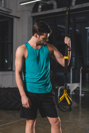Sportsman standing with suspension straps in gymの写真素材