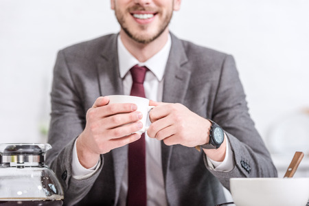 Cropped view of smiling businessman drinking coffee in kitchenの写真素材