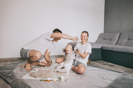 Happy young family with cute infant child painting together on floorの写真素材