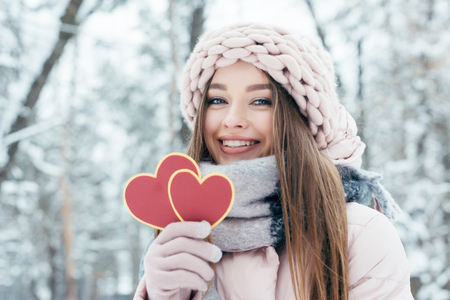 Portrait of beautiful young woman with hearts in hand looking at camera in snowy parkの写真素材
