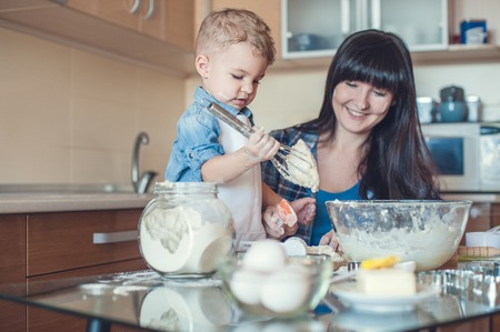 Adorable son taking dough with whisk in kitchenの写真素材