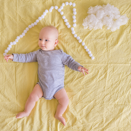 Top view of adorable infant child lying under house roof made of cotton balls and cotton cloud on...