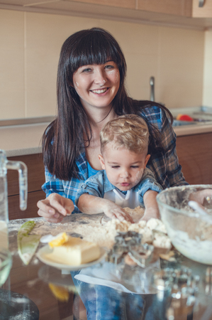 Smiling mother looking at camera and son playing with doughの写真素材