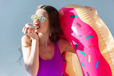 Sexy attractive girl in ultra violet swimsuit eating doughnut isolated on greyの写真素材