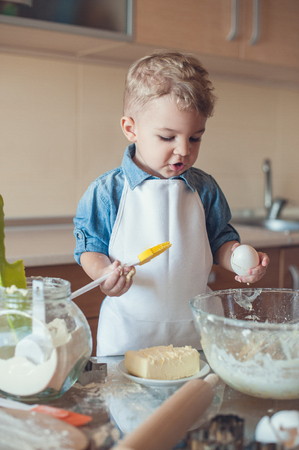 Adorable boy holding egg and cooking brush and looking downの写真素材