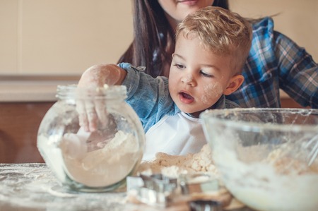 Adorable son taking flour from glass mugの写真素材