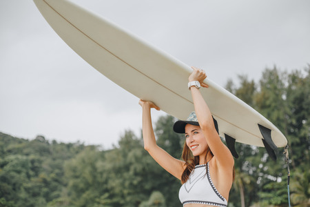 Beautiful girl in bikini holding surfboard over head