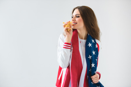 Sexy smiling girl with USA flag eating french fries isolated on whiteの写真素材