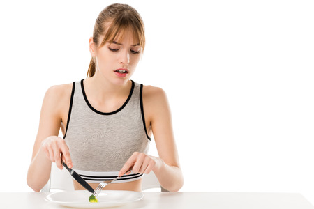 Disgusted slim woman eating piece of broccoli from plate isolated on whiteの写真素材