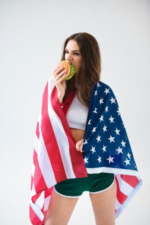 Sexy girl in USA flag eating burger isolated on whiteの写真素材