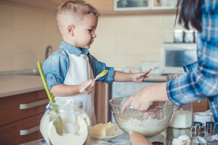Adorable son holding cooking brush and mother kneading doughの写真素材