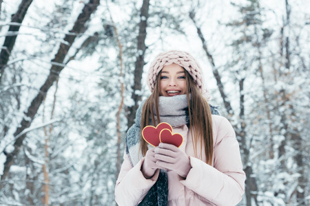 portrait of beautiful young woman with hearts in hands looking at camera in snowy parkの写真素材