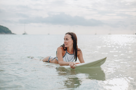 beautiful young woman in swimsuit lying on surfboard in water