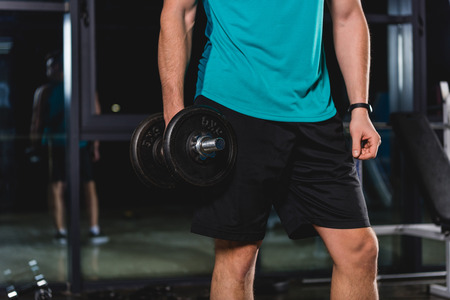 cropped view of muscular sportsman holding dumbbell in gymの写真素材