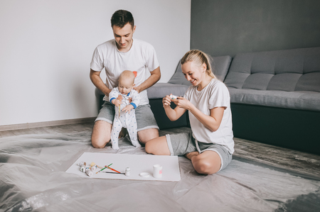 happy young family with little infant child painting together on floor at homeの写真素材