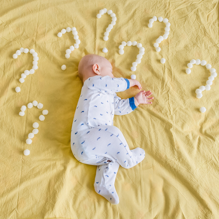 top view of infant child surrounded with question marks made of cotton balls sleeping on side in bed