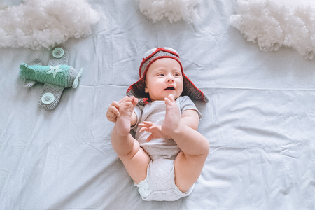 top view of dreamy infant child in pilot hat with toy plane surrounded with clouds made of cotton in bedの写真素材