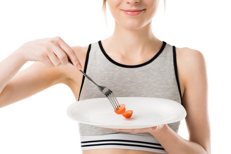 Cropped shot of smiling slim woman eating tiny cherry tomato from plate isolated on whiteの写真素材