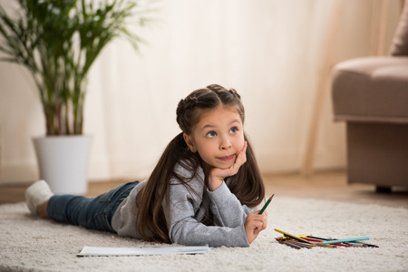 Adorable little child lying on carpet and drawing with colored pencilsの写真素材