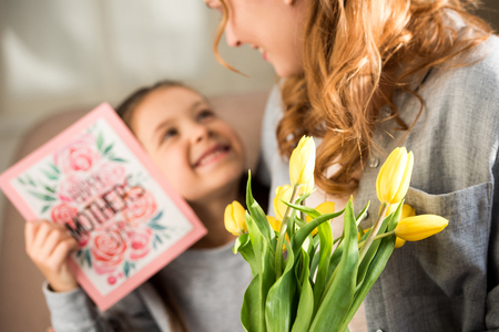 Selective focus of mother and daughter holding yellow tulips and happy mothers day greeting cardの写真素材