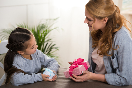 Beautiful happy mother and daughter holding gift boxes at homeの写真素材