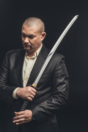 Man in suit with katana sword isolated on blackの写真素材
