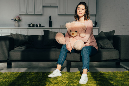beautiful woman sitting on sofa with pink teddy bear in living room at homeの写真素材