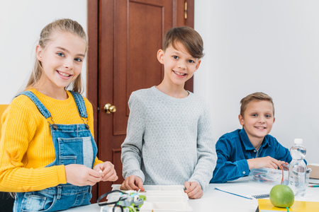 happy classmates at desk looking at camera and working in STEM classroom