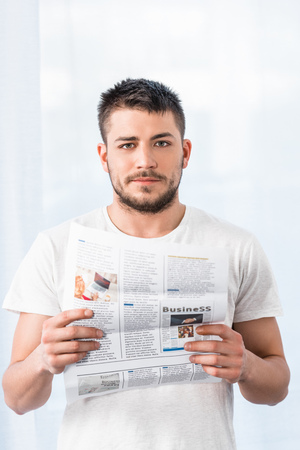 handsome man holding newspaper and looking at camera in morning at homeの写真素材
