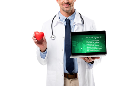 cropped view of smiling doctor holding heart model and laptop with health data on screen isolated on white, heart healthcare conceptの写真素材