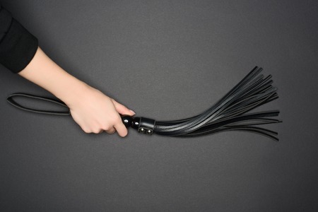 cropped view of female hand holding leather flogging whip isolated on grey