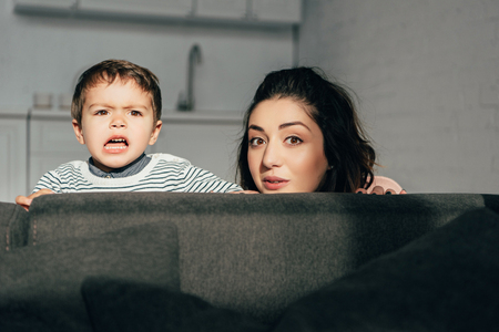 beautiful mother and emotional little son sitting on sofa at homeの写真素材
