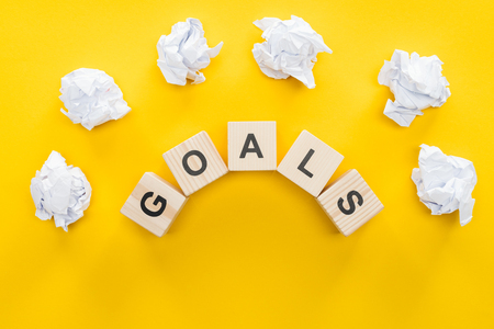 crumbled paper balls over 'goals' word made of wooden blocks on yellow background, goal setting conceptの写真素材