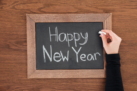partial view of woman writing 'happy new year' text on chalk board with wooden backgroundの写真素材