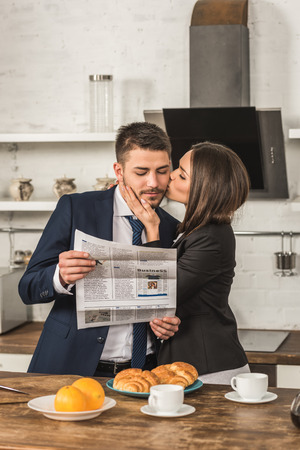 boyfriend reading newspaper and girlfriend kissing him at homeの写真素材