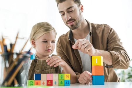 father explaining math to little daughter and playing with colorful cubes at homeの写真素材