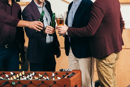 partial view of businessmen clinking drinks at table soccer in cafe