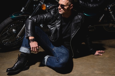 man in black sunglasses sitting by motorcycle in garage