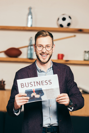 portrait of cheerful businessman showing newspaper in hands in cafeの写真素材