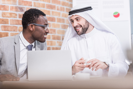 Arabian businessman looking at african american partner and smiling in officeの写真素材