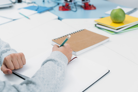 Cropped view of schoolboy sitting at desk and writing in notebook during lessonの写真素材