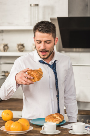 handsome man eating croissant in morning at kitchenの写真素材
