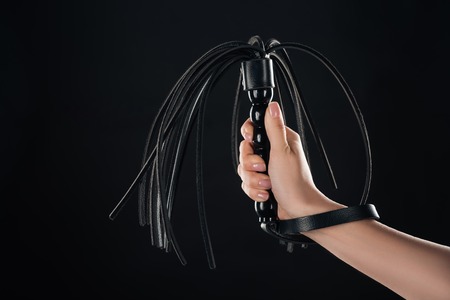cropped view of female hand holding leather flogging whip isolated on black