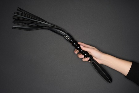 cropped view of female hand holding flogging whip isolated on grey