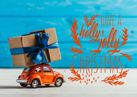 close-up shot of toy car with gift box on blue wooden background with "have a holly jolly christmas" inspirationの写真素材