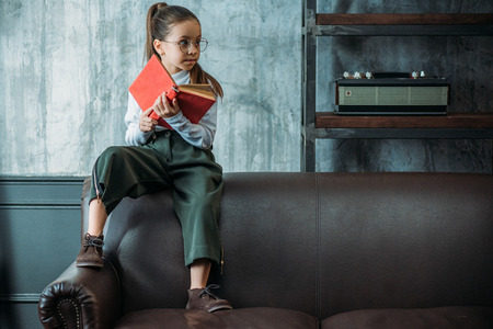 thoughtful little child with book sitting on couch in loft apartmentsの写真素材